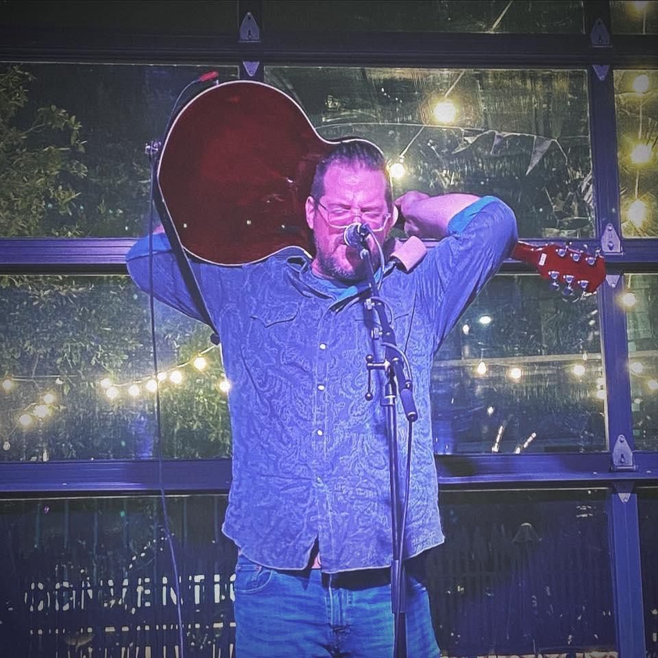 Wilhyme singing with a guitar slung behind his head under blue light