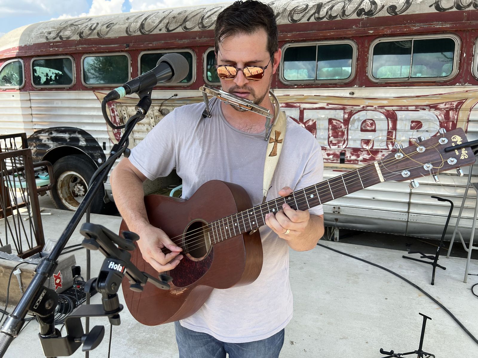 Wilhyme playing acoustic guitar and harmonica outdoors in front of a vintage bus
