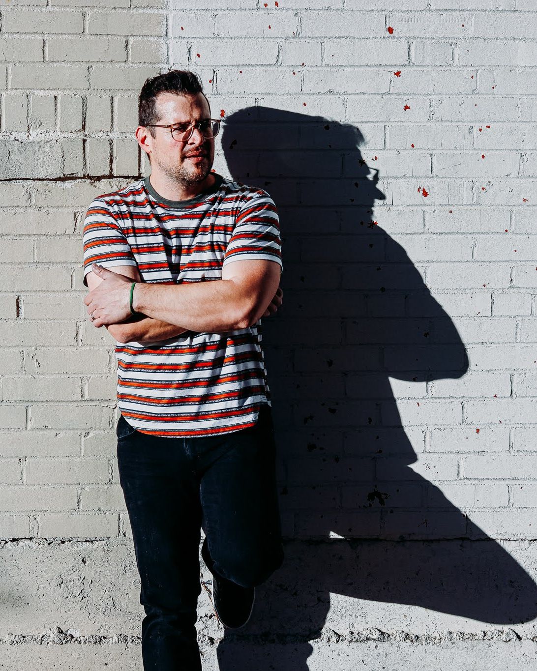 Dave Koenig of Wilhyme leaning on a sunlit white brick wall, arms crossed